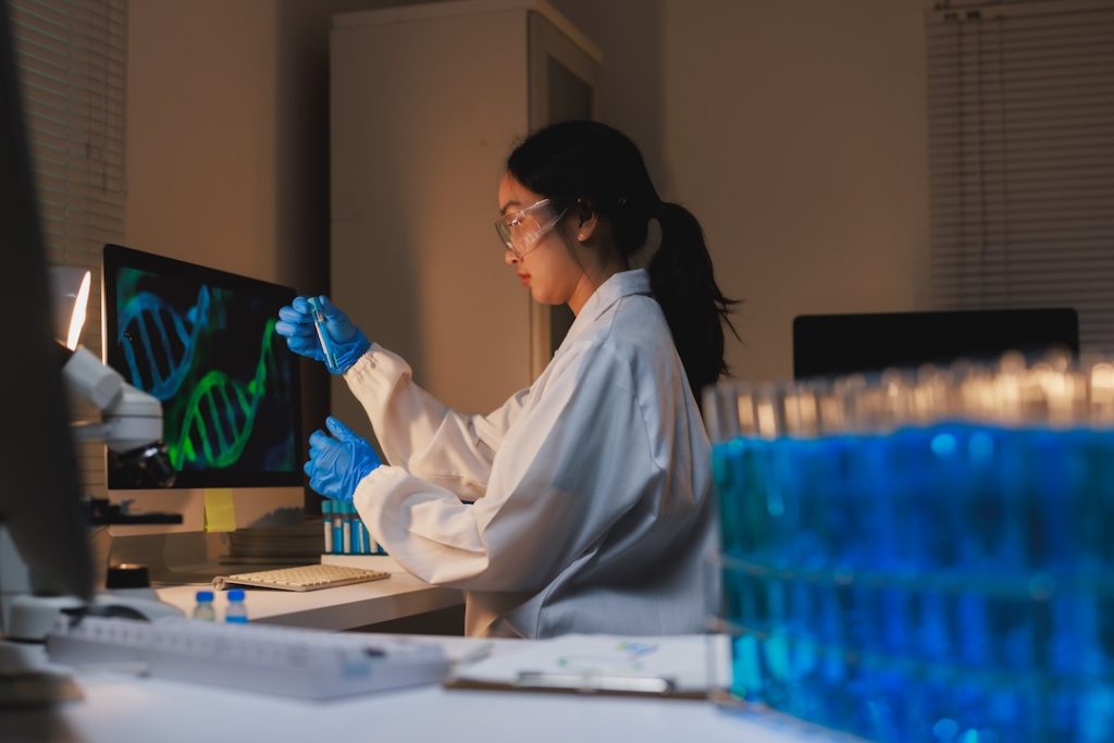Female scientist in lab coat performing molecular biology research with dna models on screen