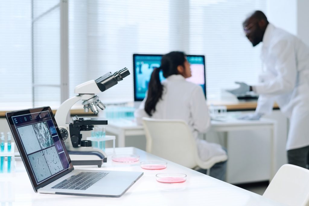Laptop, microscope and group of petri dishes standing on workplace of contemporary researcher or virologist in clinical laboratory