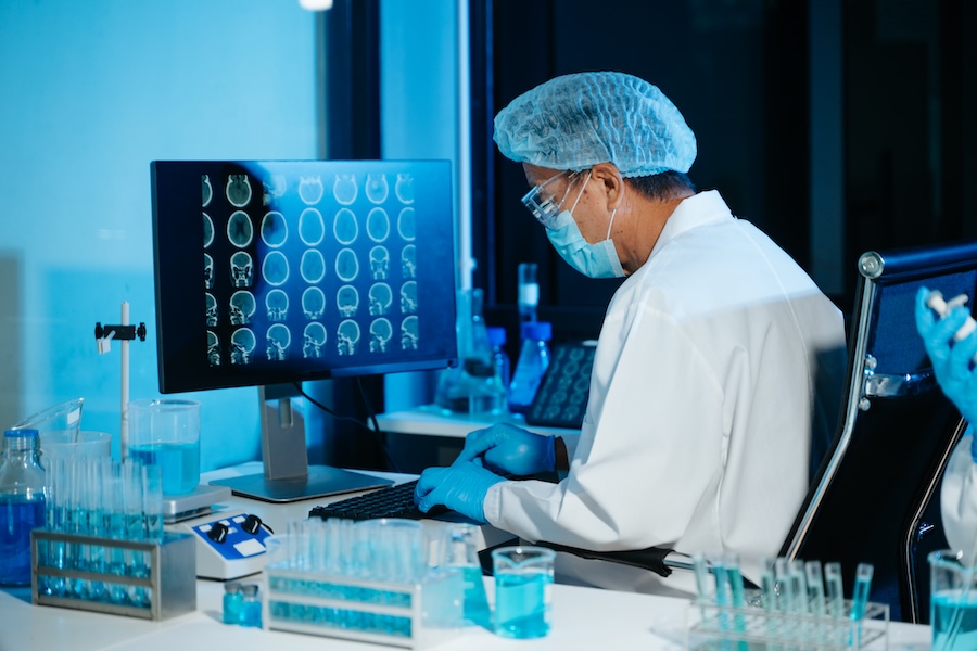 Medical scientist working in laboratory, analyzing brain scan images on computer for diagnostics and research, reflecting healthcare technology, data analysis and professional lab environment.