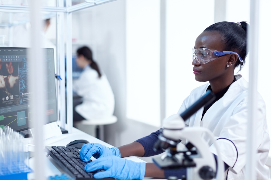 Professional african medical worker typing information about virus study Black healthcare scientist in biochemistry laboratory wearing sterile equipment.